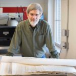 Image of Tim Barrett in paper studio, with several sheets of paper in the foreground.