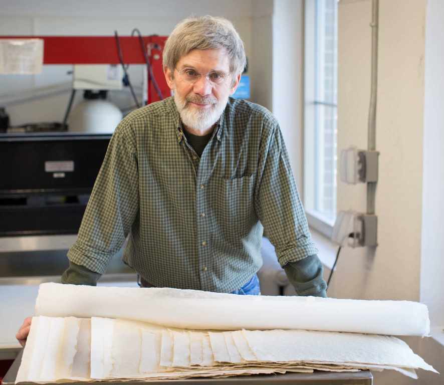 Image of Tim Barrett in paper studio, with several sheets of paper in the foreground.